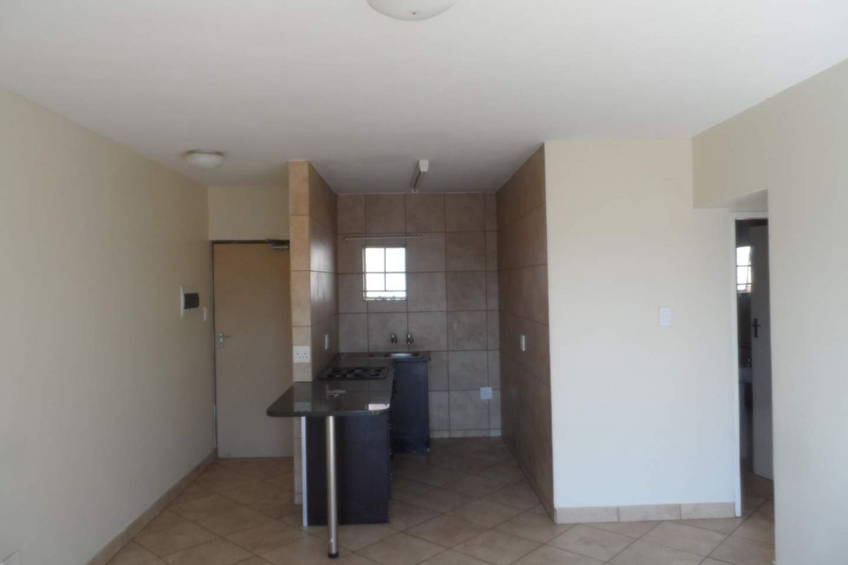 A compact, empty kitchen area featuring tiled flooring, a breakfast bar, built-in cabinetry, and a gas hob, ready for a modern update.