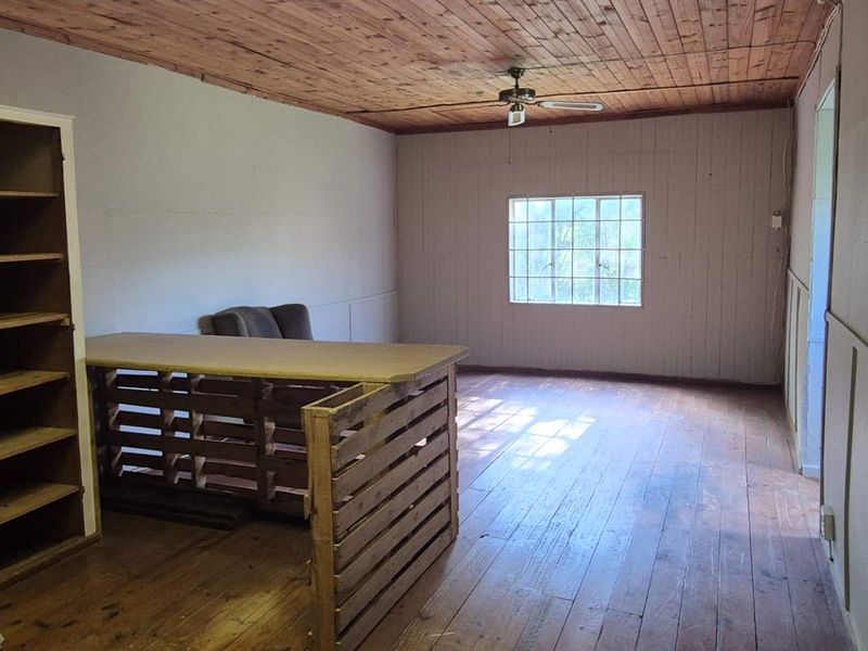 A living area featuring timber ceilings and flooring, with a ceiling fan and grid window, offering a rustic aesthetic in need of modernization.