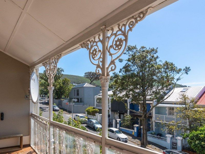 A covered balcony featuring classic wrought iron decorative columns and balustrade, offering an elevated view of the surrounding streetscape and neighborhood.