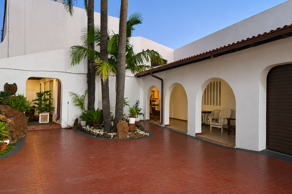 A well-maintained rear courtyard featuring a red brick paved area, arched covered patio spaces, and established palm trees.