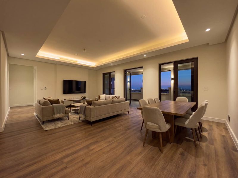 Spacious open-plan living and dining area featuring modern recessed cove lighting, high-quality laminate flooring, and direct access to a balcony with evening views.