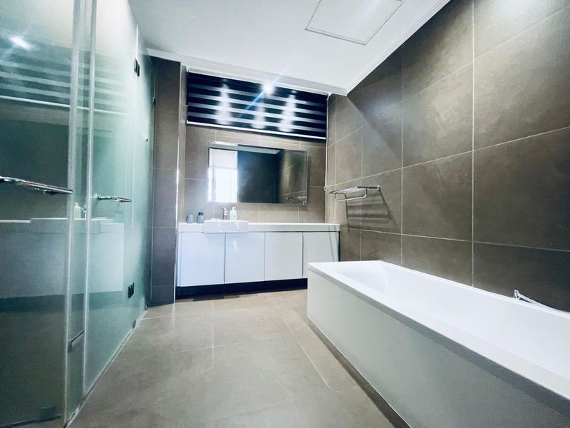 Modern bathroom featuring a glass shower enclosure, a white vanity cabinet with a mirror, and a bathtub, finished with neutral wall and floor tiles.