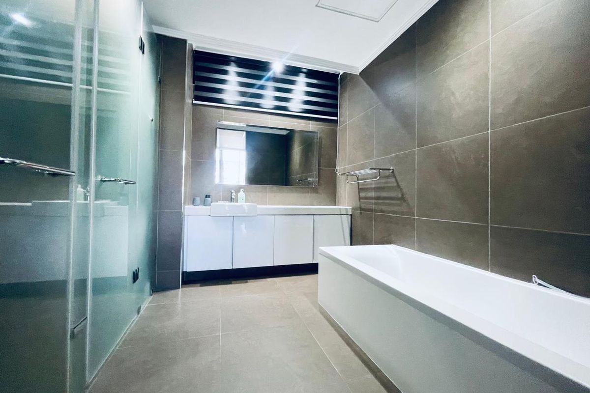 Modern bathroom featuring a glass shower enclosure, a white vanity cabinet with a mirror, and a bathtub, finished with neutral wall and floor tiles.