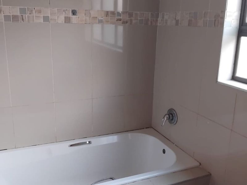 A clean, neutral-toned bathroom featuring a built-in bathtub with chrome fixtures and decorative mosaic tile accents.