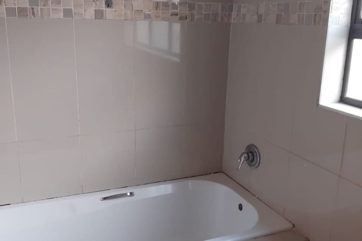 A clean, neutral-toned bathroom featuring a built-in bathtub with chrome fixtures and decorative mosaic tile accents.