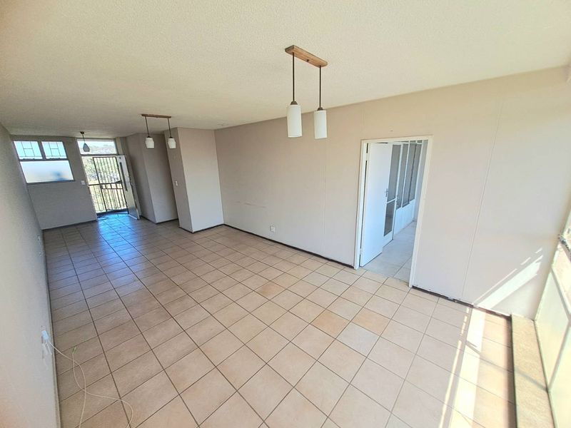 Spacious, empty living area featuring neutral tiled flooring, pendant lighting, and access to an outdoor balcony through a security gate.
