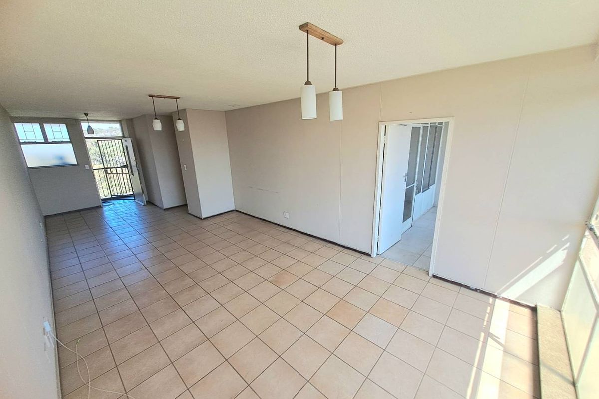 Spacious, empty living area featuring neutral tiled flooring, pendant lighting, and access to an outdoor balcony through a security gate.