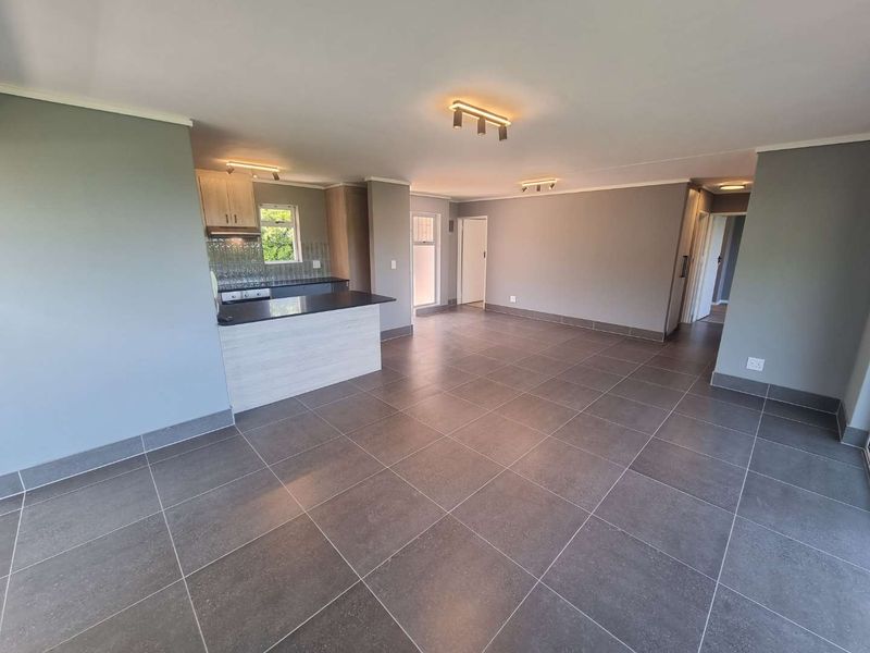 Spacious open-plan living area featuring modern grey floor tiles, neutral walls, and a functional kitchen with built-in cabinetry and appliances.
