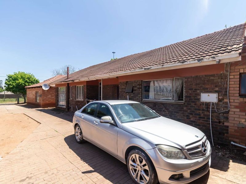 Front exterior view of a single-story brick house featuring a tiled roof and paved driveway area.