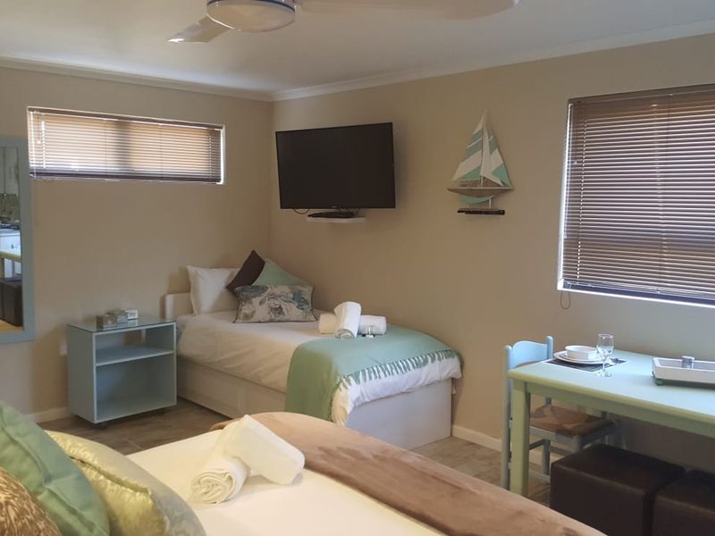 A functional bedroom featuring tiled flooring, ceiling fan, and venetian blinds, with a view into the adjacent kitchen area.