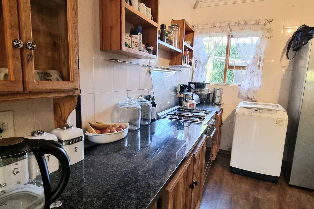 A functional kitchen featuring dark granite countertops, wooden cabinetry, a built-in gas hob, and tiled wall finishes.