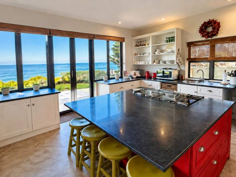 Spacious kitchen featuring a large island with gas cooktop, ample cabinetry, open shelving, and expansive windows offering stunning ocean views.
