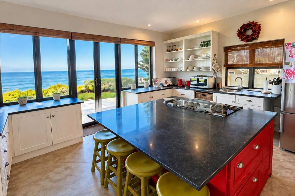 Spacious kitchen featuring a large island with gas cooktop, ample cabinetry, open shelving, and expansive windows offering stunning ocean views.