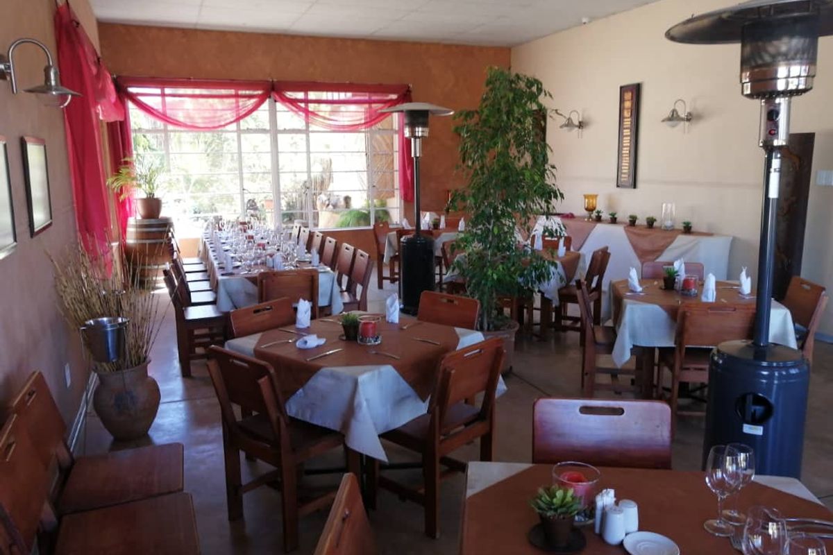 A spacious dining area featuring large windows, tiled flooring, and wall-mounted lighting fixtures, suitable for restaurant or event hosting.