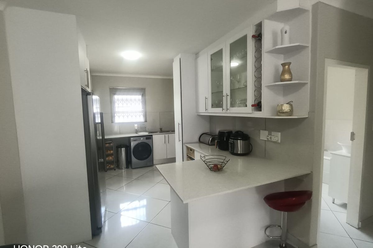 Modern kitchen featuring white cabinetry, stone countertops, a breakfast bar, and tiled flooring, with an adjacent laundry area and integrated storage.