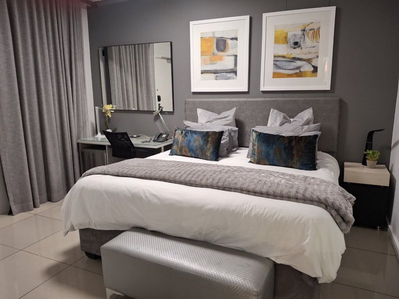 A well-maintained bedroom featuring neutral tiled flooring, a modern grey accent wall, and integrated curtain tracks.