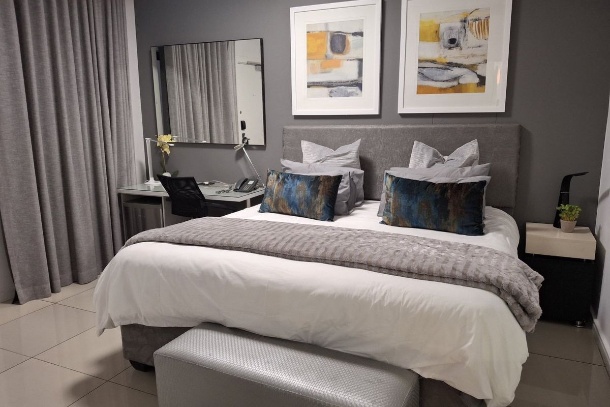 A well-maintained bedroom featuring neutral tiled flooring, a modern grey accent wall, and integrated curtain tracks.