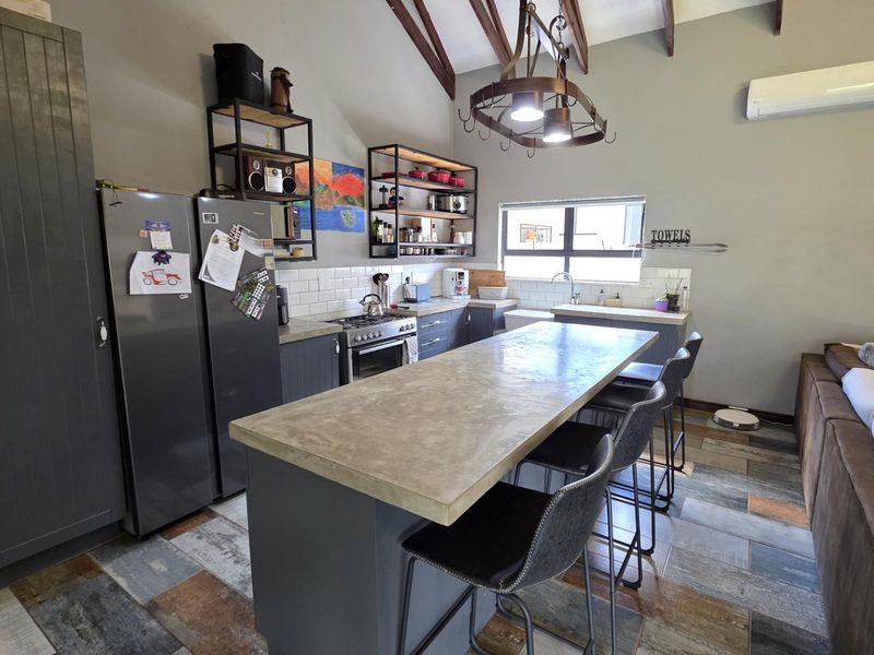 Spacious open-plan kitchen and living area featuring exposed timber beams, a central concrete-topped island, modern cabinetry, and durable ceramic tile flooring.
