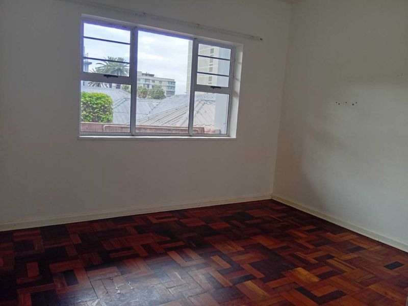 An empty bedroom featuring traditional parquet flooring and a large window providing natural light and an urban view.