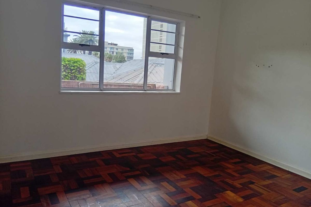 An empty bedroom featuring traditional parquet flooring and a large window providing natural light and an urban view.
