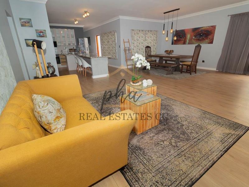 Spacious open-plan living and dining area featuring modern laminate flooring, a central kitchen island with granite countertops, and elegant pendant lighting.