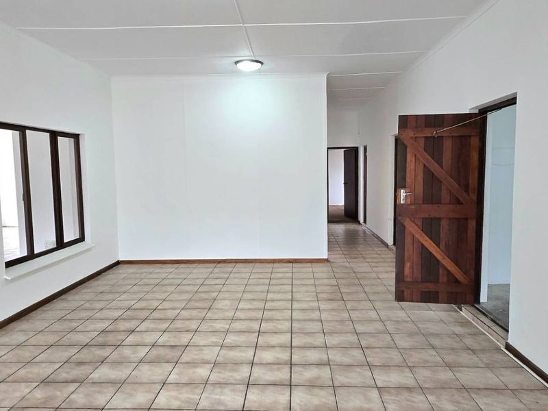 A spacious, empty living area featuring neutral tiled flooring, white walls, and traditional timber doors, offering a blank canvas for interior design.