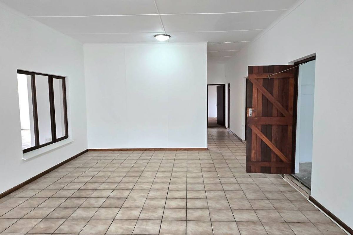 A spacious, empty living area featuring neutral tiled flooring, white walls, and traditional timber doors, offering a blank canvas for interior design.