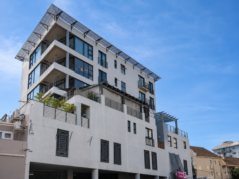 A modern multi-story apartment building featuring tiered balconies, pergola structures, and large glass windows, showcasing contemporary architectural design.
