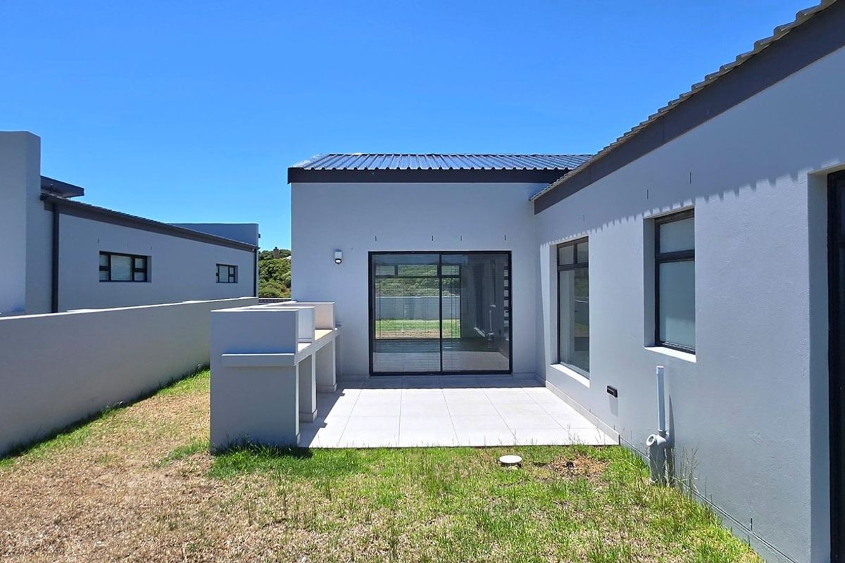 Rear exterior view featuring a paved patio area with a built-in braai, sliding glass doors, and a surrounding boundary wall.