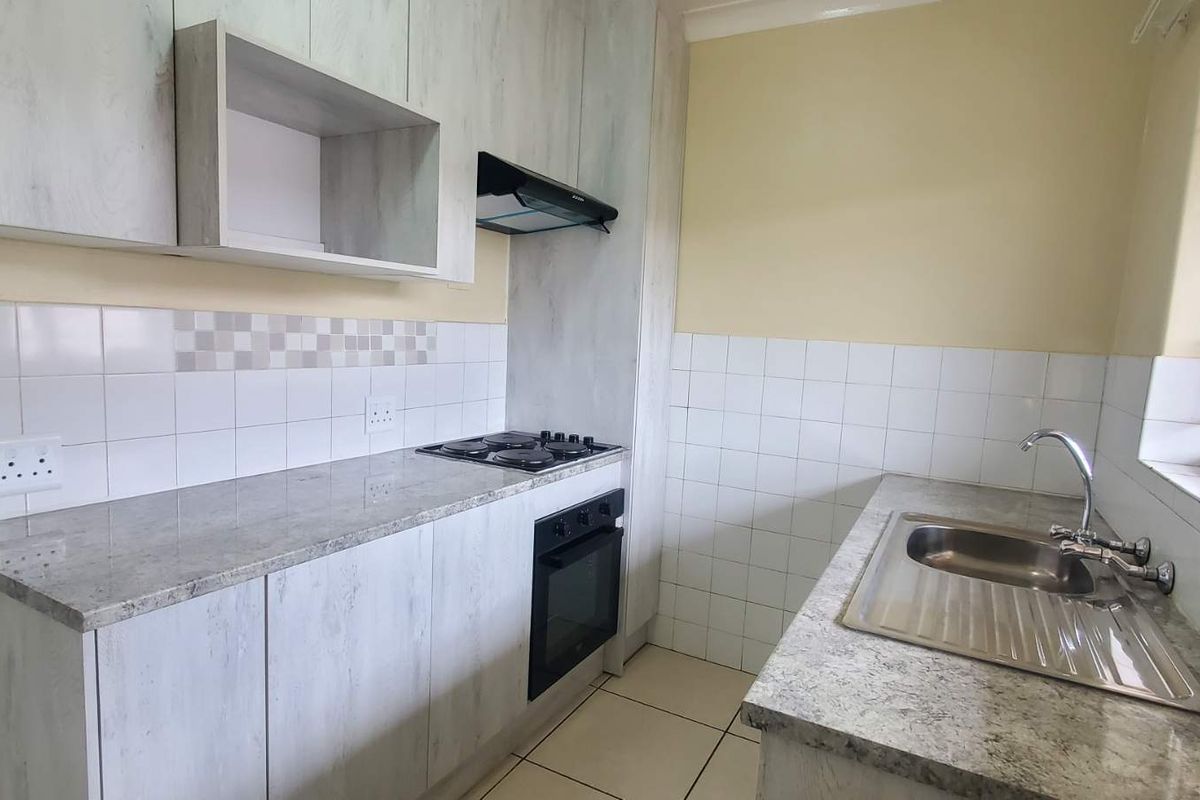 Functional kitchen featuring light-toned cabinetry, granite-look countertops, a built-in oven, hob, extractor fan, and a stainless steel sink with tiled splashbacks.