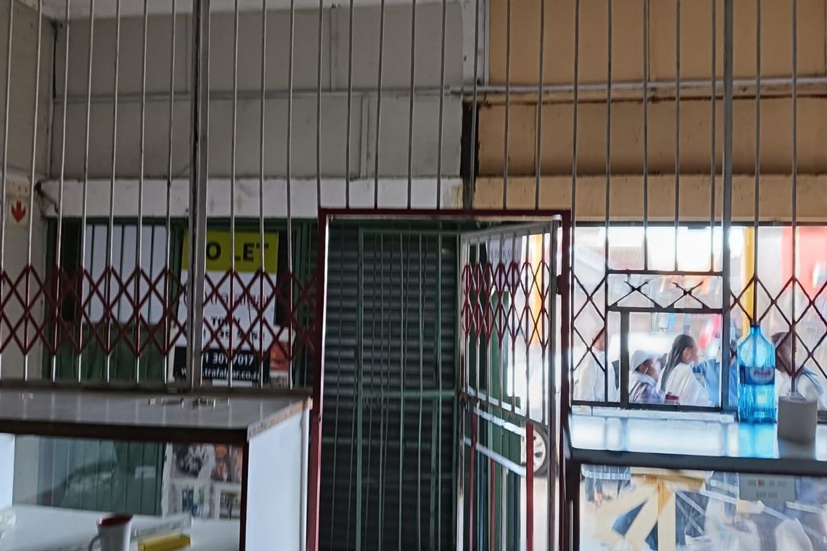 Commercial entrance area featuring heavy-duty security gates and roller shutters, showing signs of wear and dated finishes.