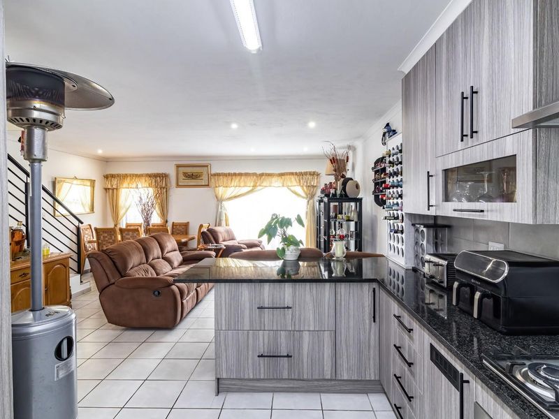 Open-plan living area featuring a modern kitchen with granite countertops, gas hob, and tiled flooring, seamlessly flowing into the adjacent dining and lounge space.
