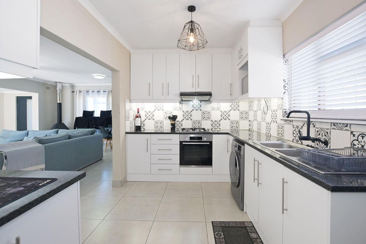 Modern kitchen featuring white cabinetry, patterned tile backsplash, integrated oven, hob, extractor fan, and a double sink with a black faucet.