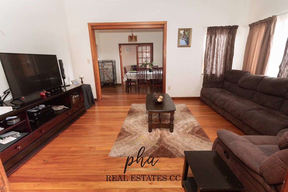 Spacious living room featuring polished hardwood flooring and timber door frames, leading through to an adjacent dining area with classic french doors.