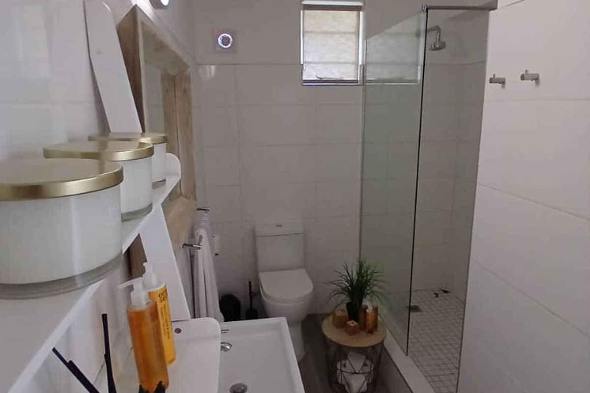 A modern, clean bathroom featuring a walk-in shower with a glass screen, wall-mounted basin, and white tiled finishes.