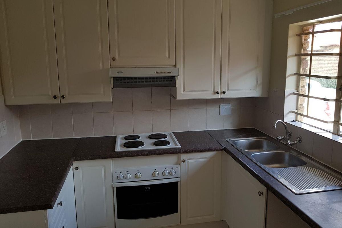 A functional kitchen featuring built-in cabinetry, laminate countertops, an electric hob with extractor fan, and a double bowl stainless steel sink.