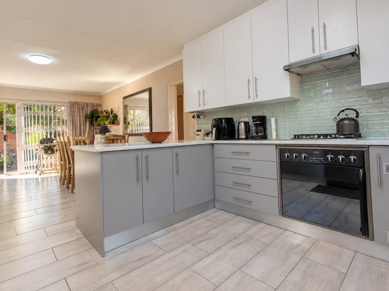 Modern open-plan kitchen featuring sleek grey and white cabinetry, subway tile backsplash, and integrated appliances, flowing seamlessly into the adjacent living and dining area.