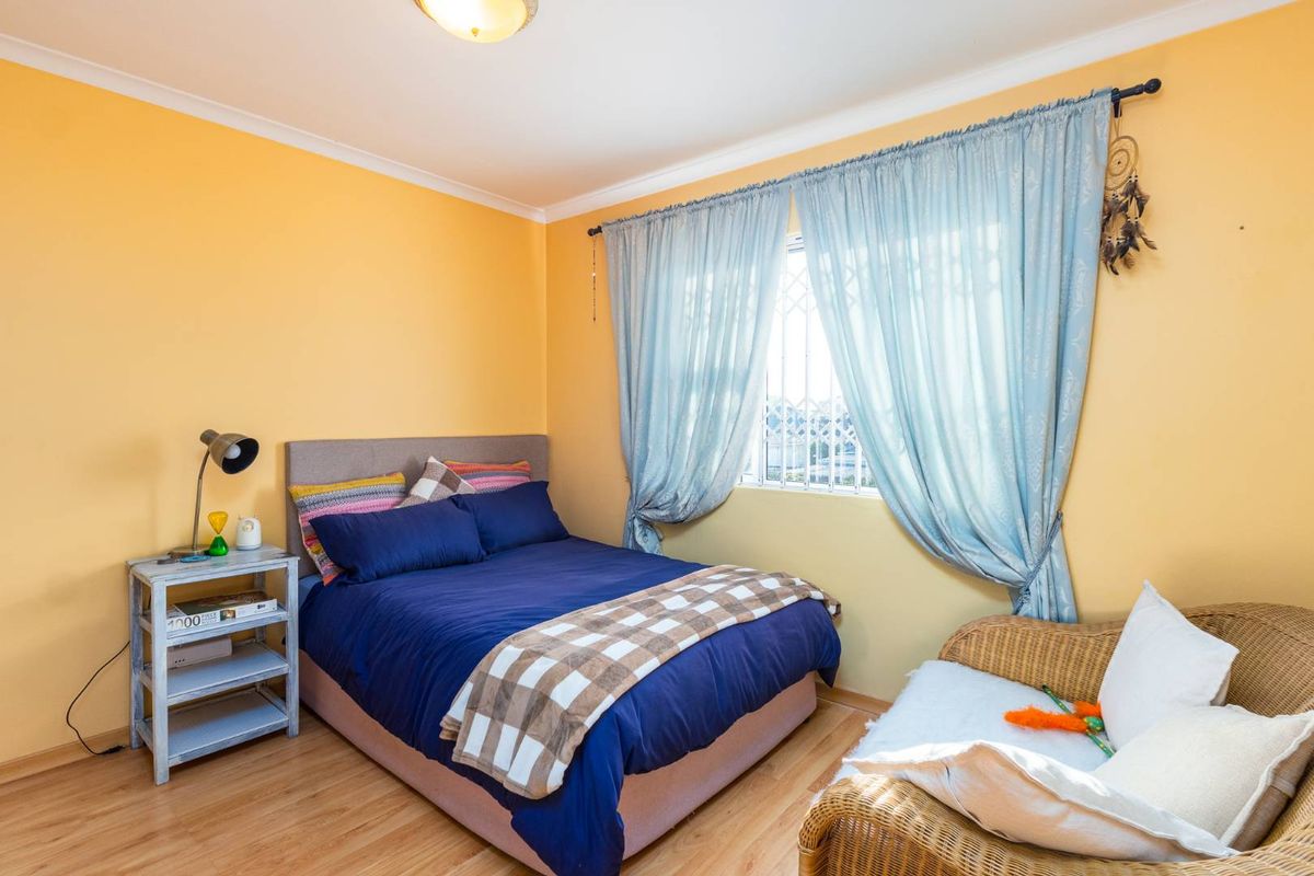 A cozy bedroom featuring laminate flooring, yellow painted walls, and a window fitted with security bars.