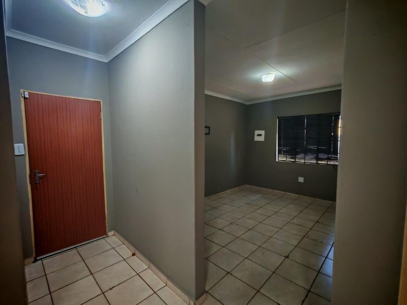 An empty living area featuring tiled flooring, neutral grey walls, and venetian blinds, offering a blank canvas for interior design.