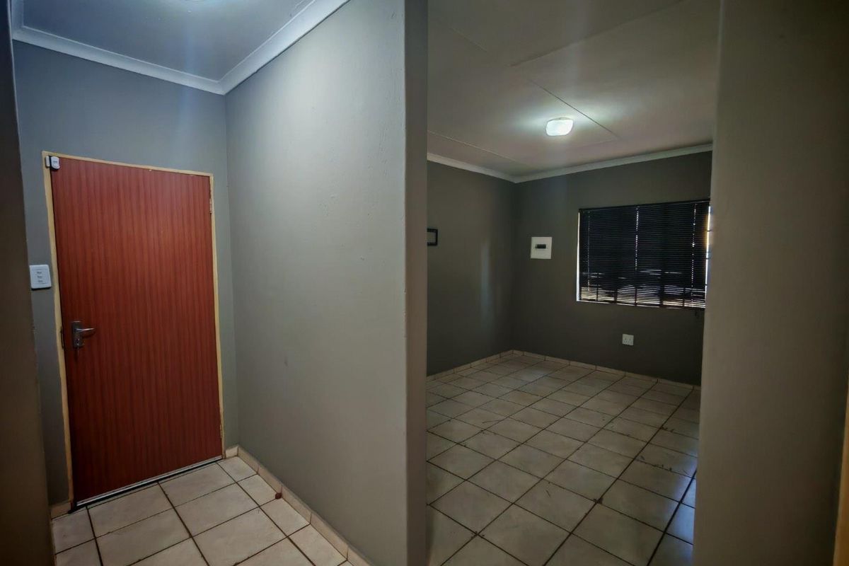 An empty living area featuring tiled flooring, neutral grey walls, and venetian blinds, offering a blank canvas for interior design.