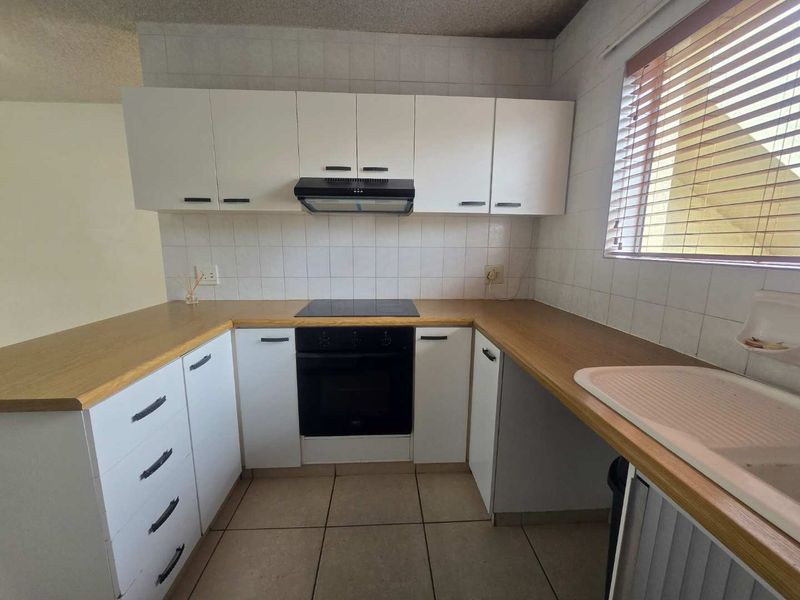 A functional kitchen featuring white cabinetry, laminate countertops, a built-in oven with hob, and tiled flooring.