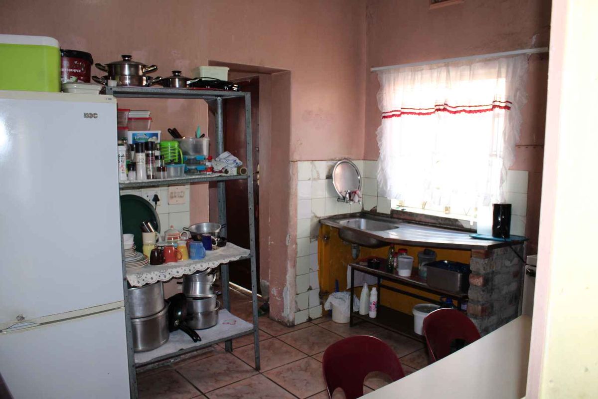 A dated kitchen area featuring a basic stainless steel sink, tiled splashback, and tiled flooring, requiring significant cosmetic updates and renovation.