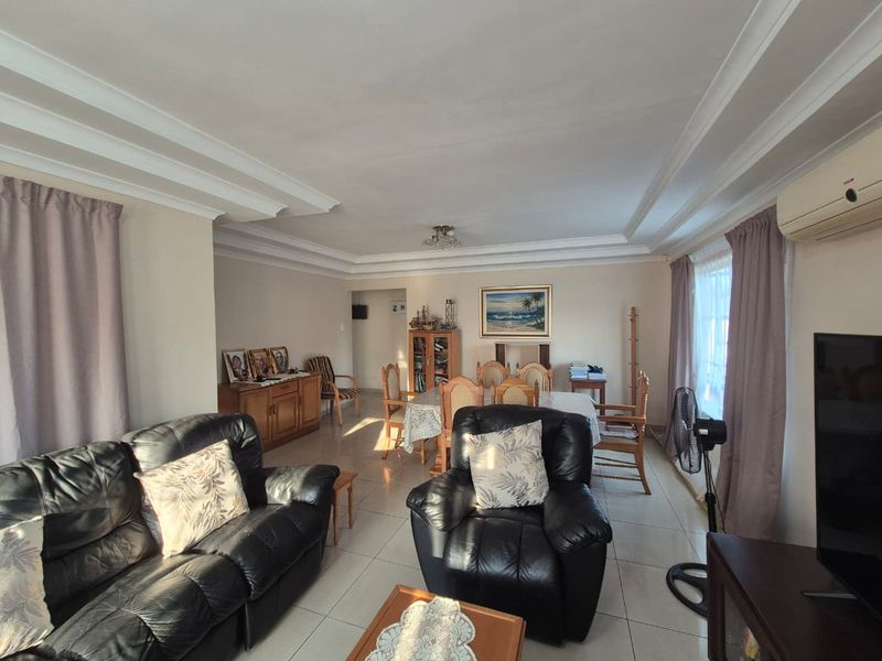 Spacious open-plan living and dining area featuring tiled flooring, decorative ceiling cornices, and a wall-mounted air conditioning unit.