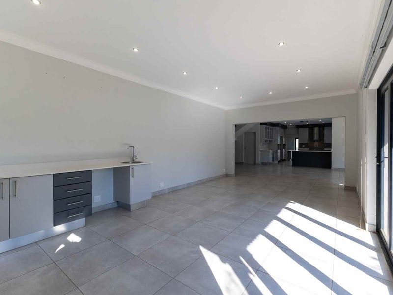 Spacious open-plan living area featuring tiled floors, recessed lighting, and a built-in wet bar or kitchenette, leading to an adjacent kitchen space.