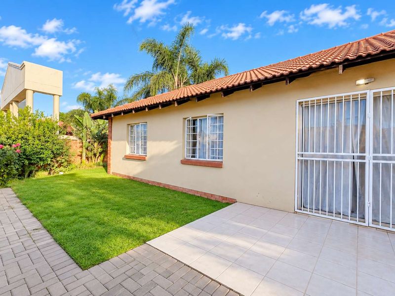 Rear exterior view of the townhouse featuring a tiled patio, paved walkway, well-maintained lawn, and secure window and door fittings.