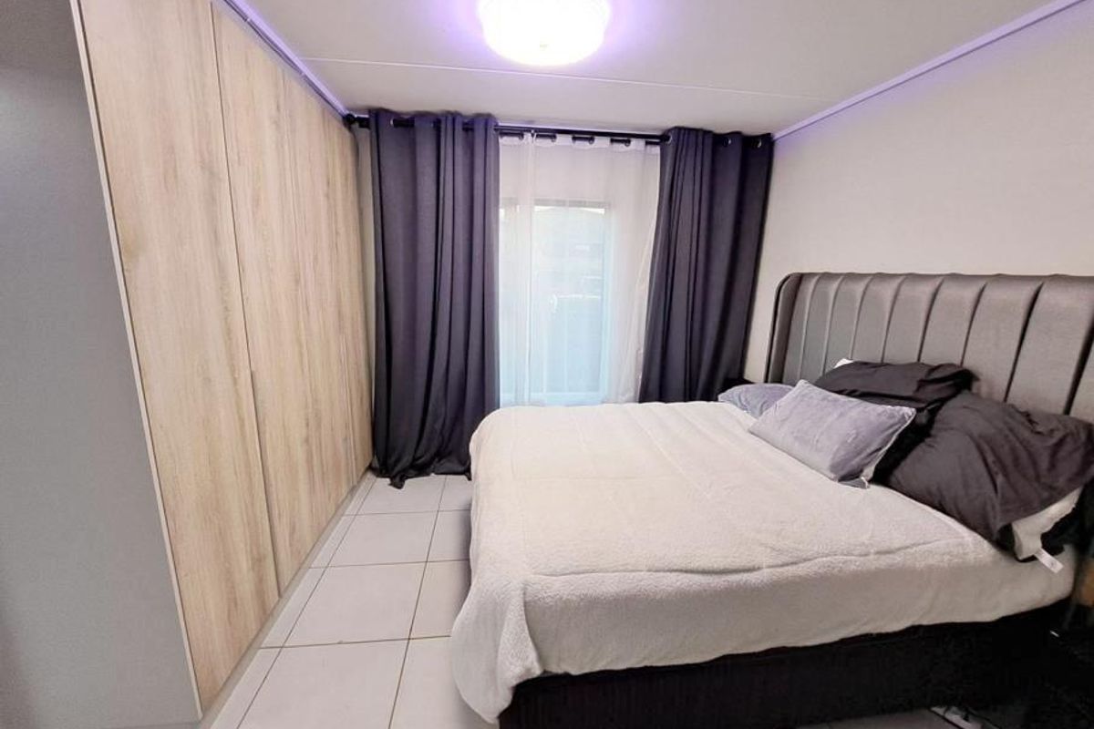 A well-maintained bedroom featuring light wood-finish built-in cupboards, neutral tiled flooring, and a modern ceiling light fixture.