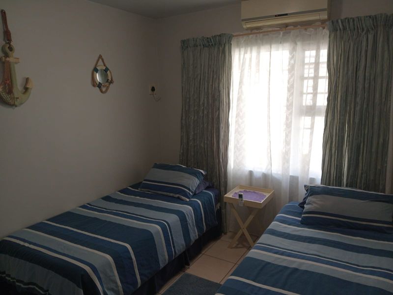 A functional bedroom featuring tiled flooring and a wall-mounted split-system air conditioner, providing a comfortable space with natural light.