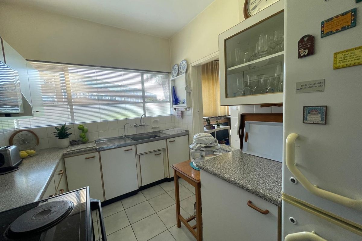 A functional kitchen featuring white cabinetry, laminate countertops, a stainless steel sink, and tiled flooring, offering a practical layout for daily meal preparation.