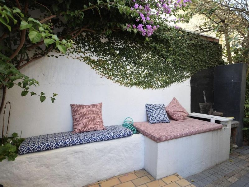 Outdoor patio area featuring built-in masonry seating and a built-in braai, set against a wall with climbing greenery.