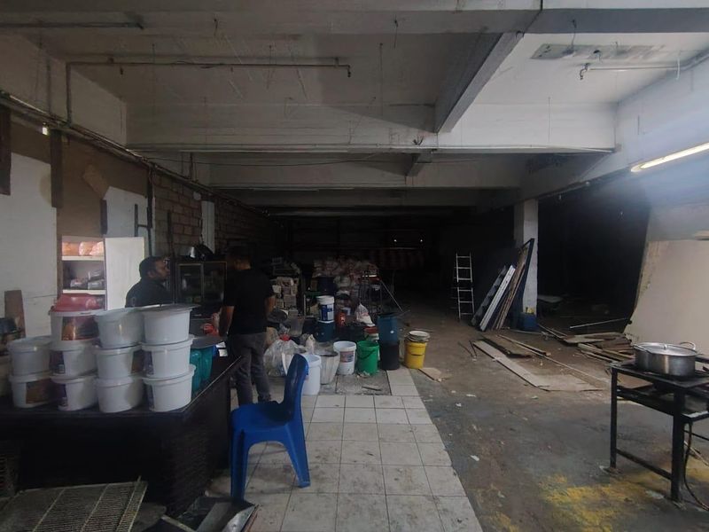 Large industrial utility space featuring exposed concrete structural elements, tiled flooring, and unfinished brick walls, suitable for storage or workshop use.